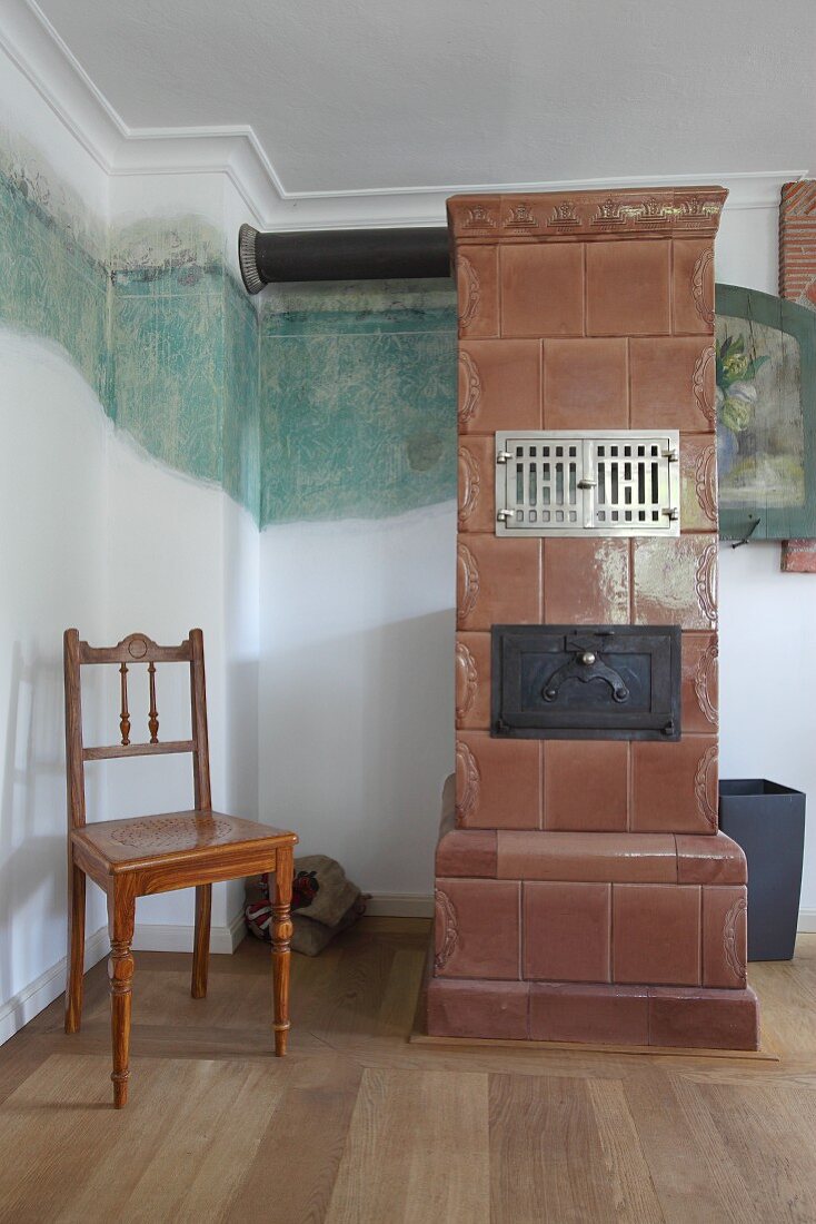 Old tiled stove against wall with partially uncovered historical mural