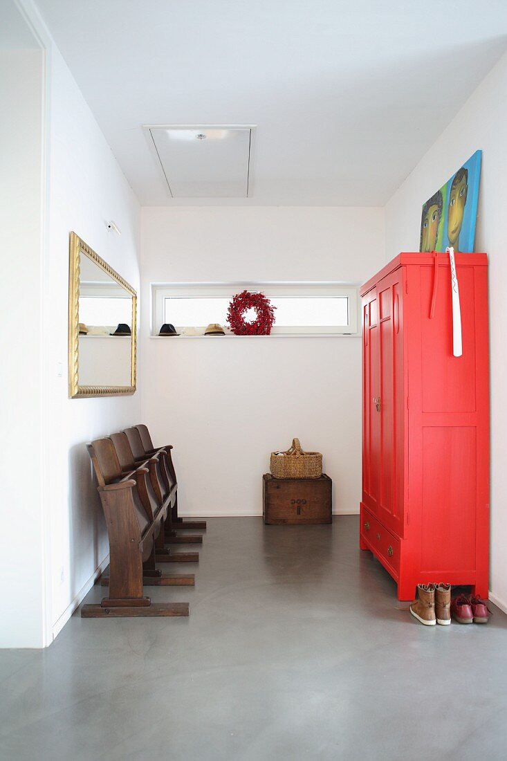 Old cinema chairs opposite bright red wardrobe in hallway with concrete floor