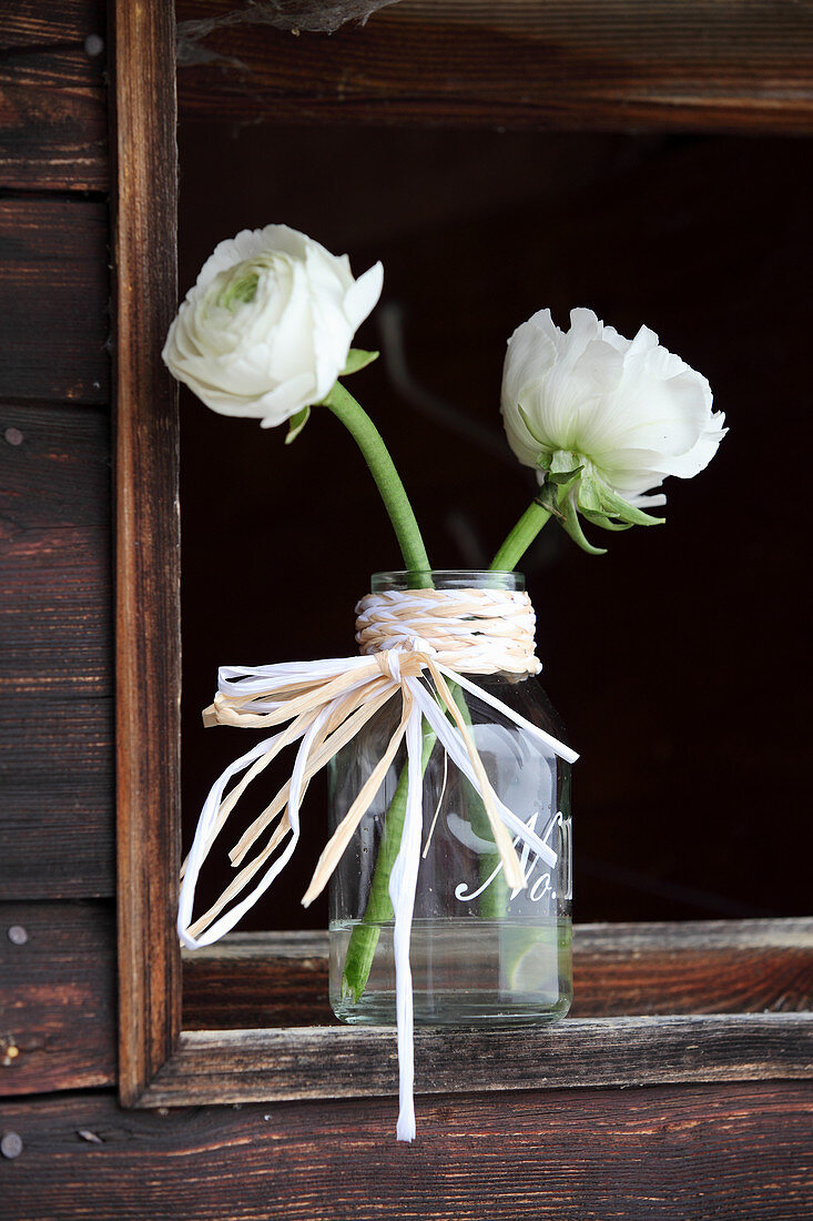 Ranunculus in glass bottle decorated with plaited raffia