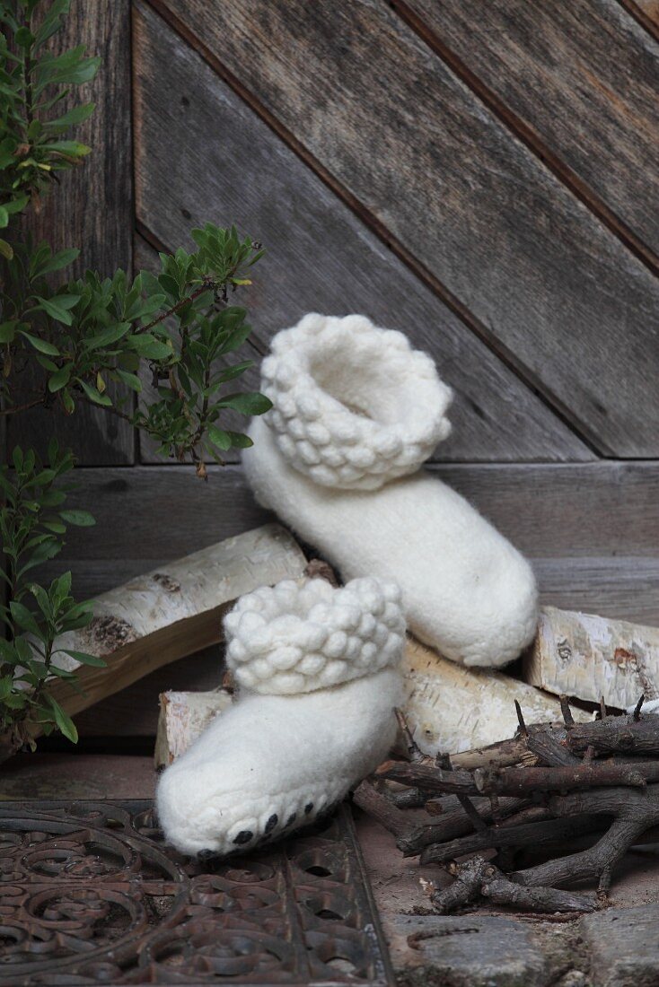 White, hand-made felt slippers in front of rustic wooden door
