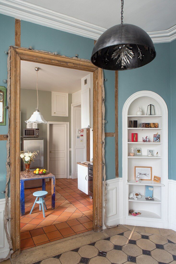 Blick vom Vorraum mit Einbauregal und blauen Wänden in die Küche