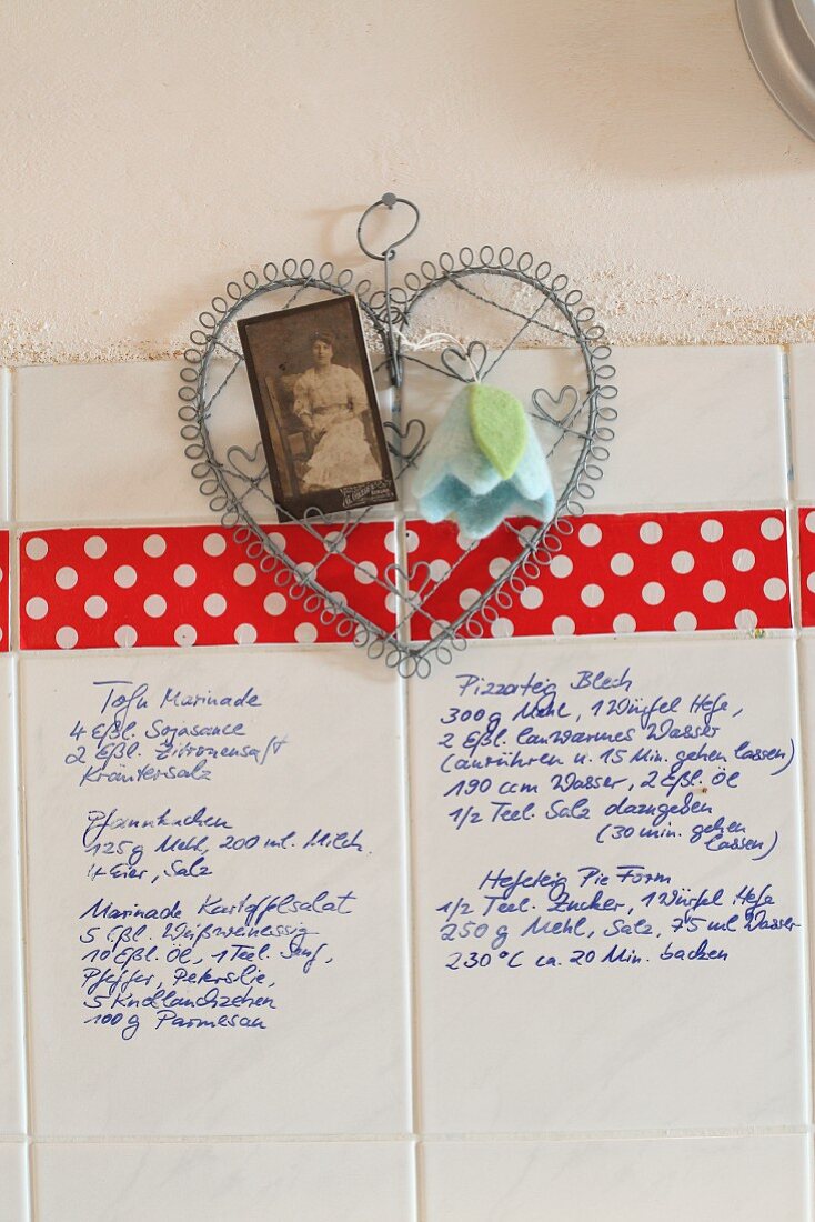 Handgeschriebene Rezepte auf weissen Wandfliesen, dekoriert mit nostalgischem Foto und Filzblüte an Drahtherz