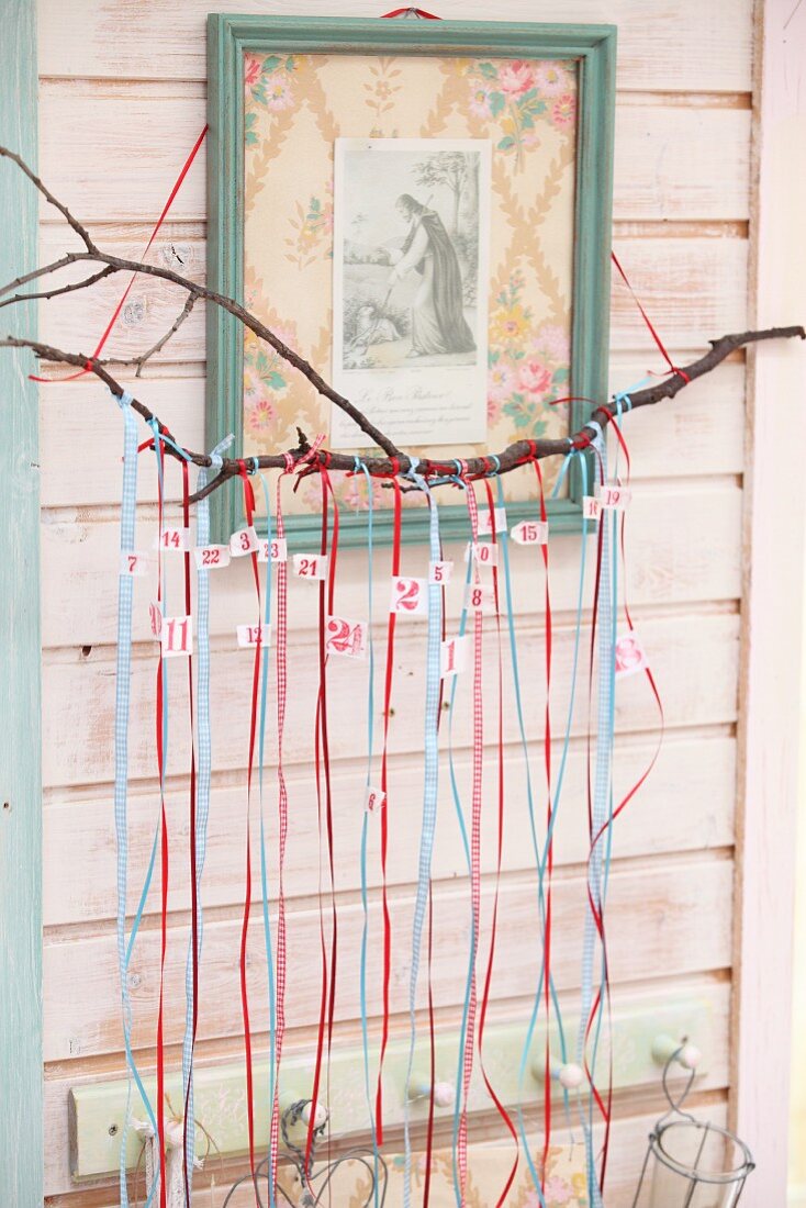 Hand-made Advent calender with numbered ribbons hung from branch below religious icon