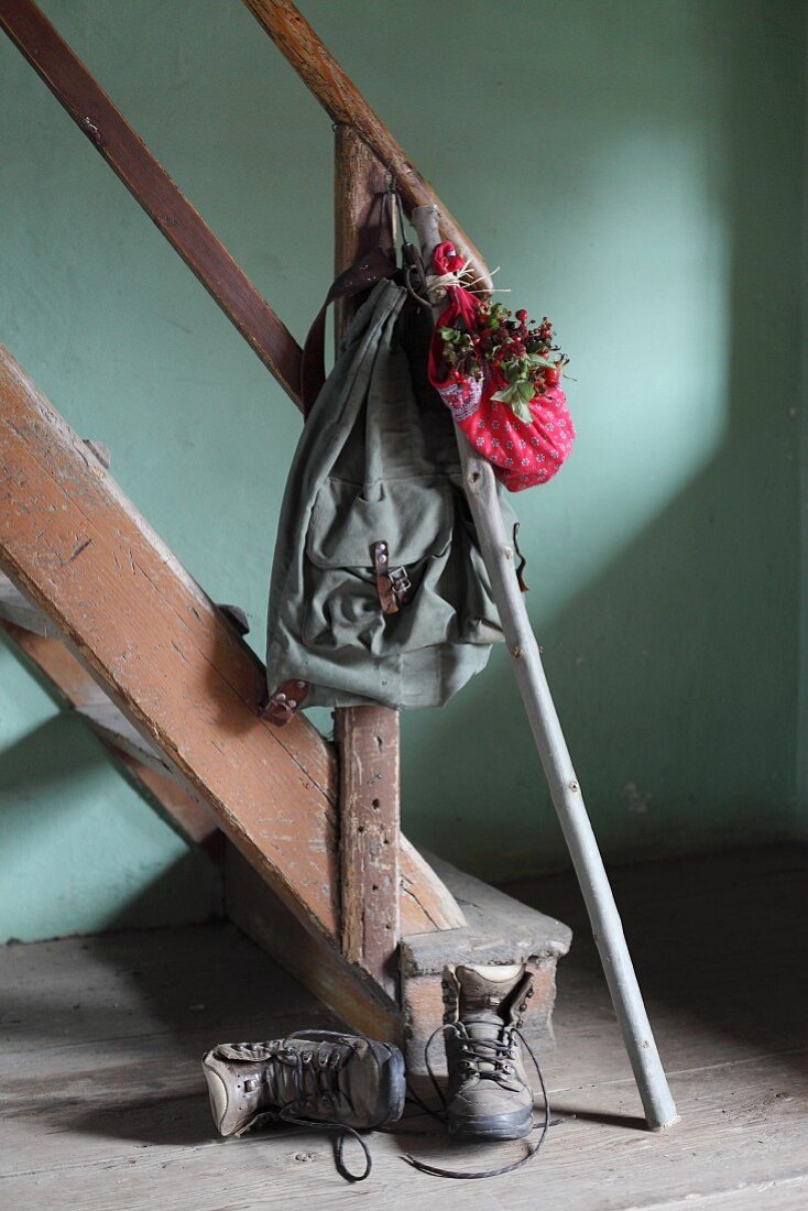 Nostalgischer Rucksack mit Wanderstock und Bündel mit roten Hagebutten an Vintage Holzstiege