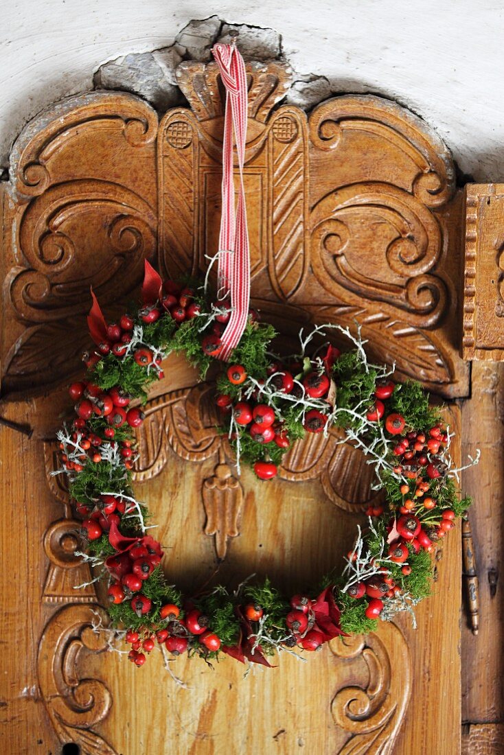 Romantic heart-shaped wreath of rose hips and moss hung on artistically carved wooden panel
