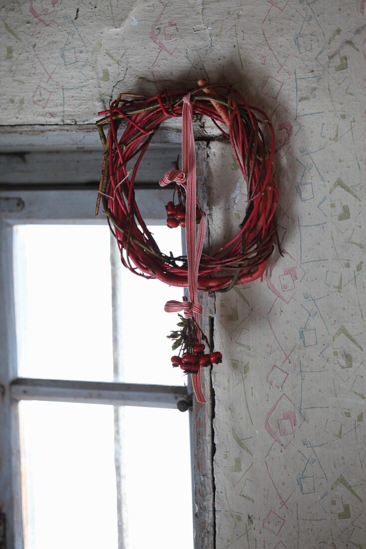 Wreath of twigs with rose-hip posy hung from red and white ribbon next to window
