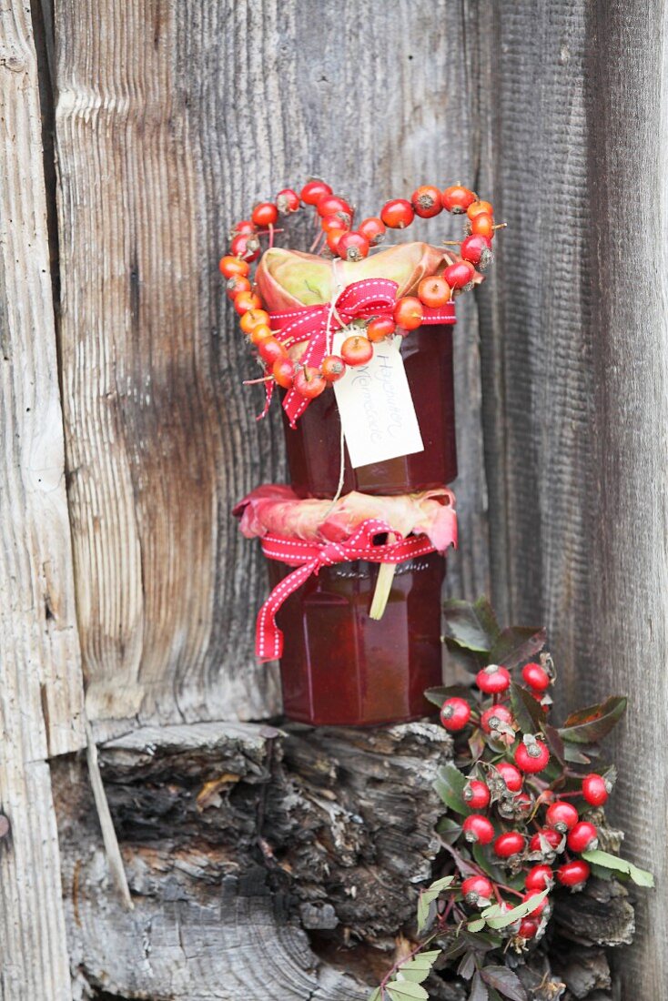 Gestapelte Marmeladegläser mit Hagebuttenherz dekoriert vor rustikaler Brettterwand