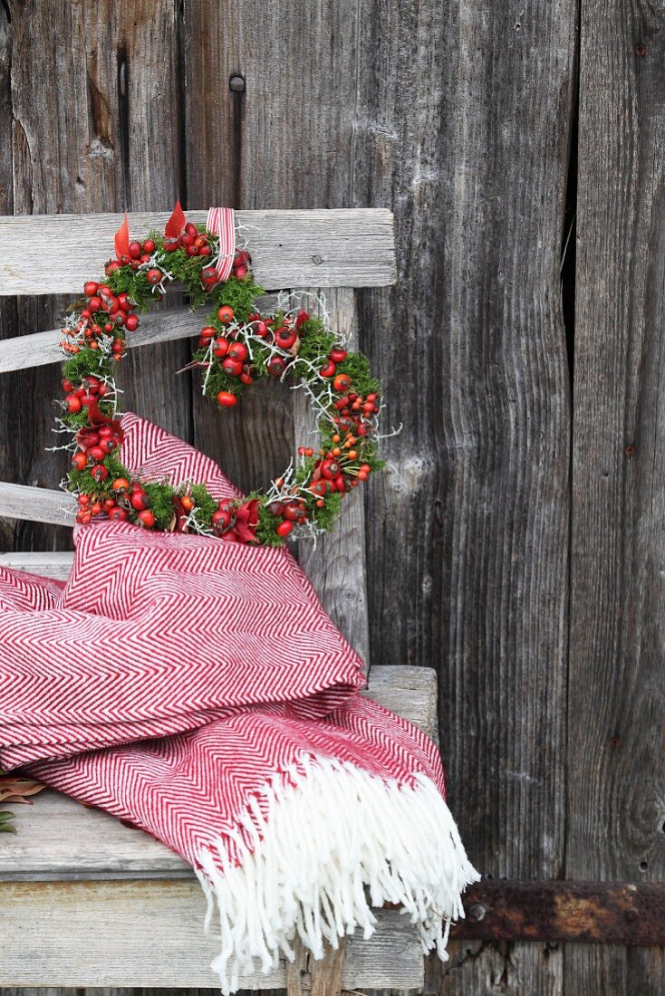 Romantic heart-shaped wreath of rose hips and moss on rustic wooden bench