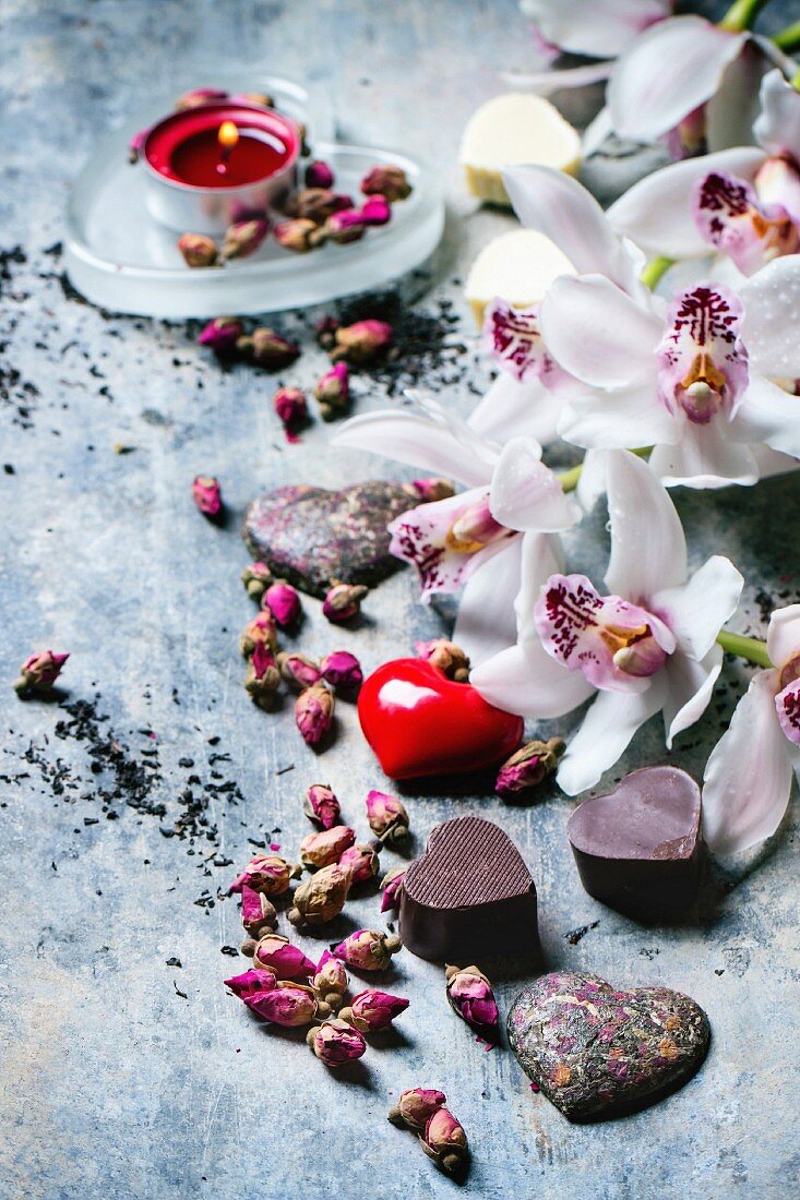 Valentinstag: Pralinen in Herzform zwischen getrockneten Teerosen und Orchideen