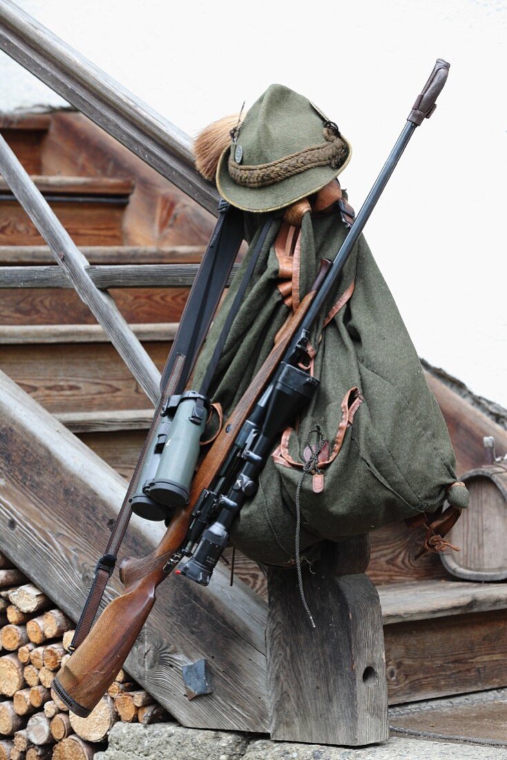 Hunting rifle, backpack, binoculars and hunting hat on newel post of rustic staircase