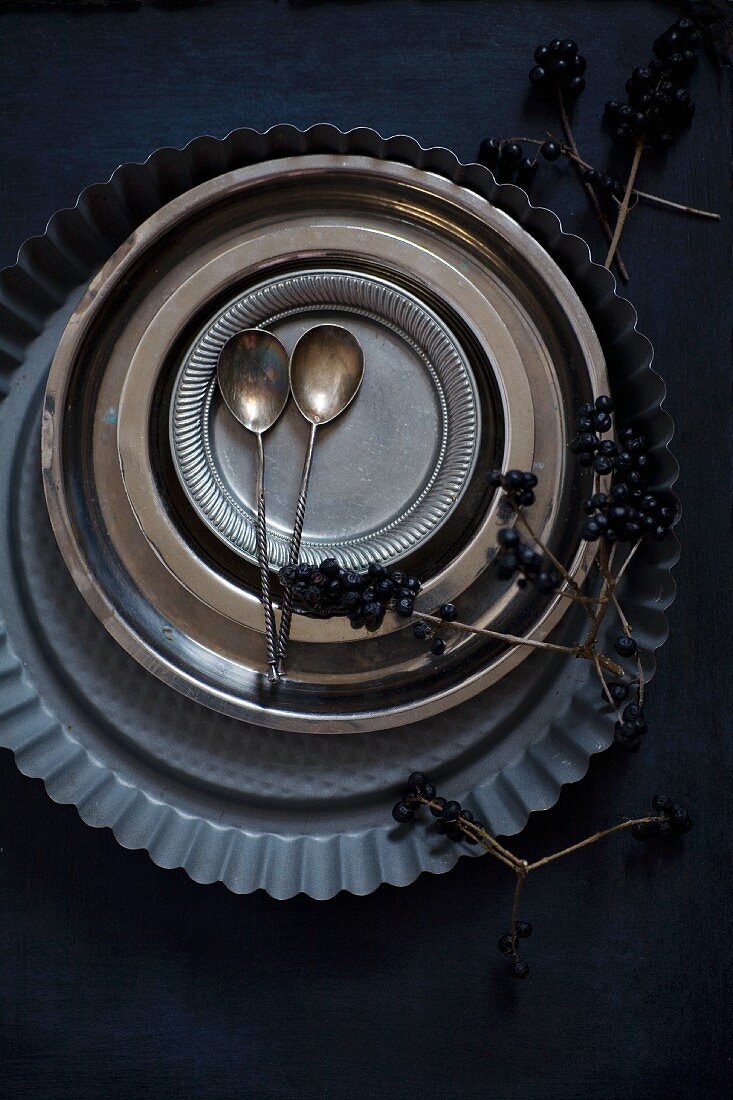 Flan tin, metal plates, pewter plates and silver spoons on black surface