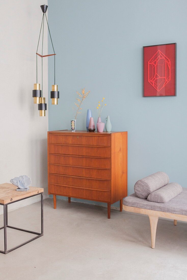 Collection of vases on chest of drawers against pale blue wall below retro pendant lamp