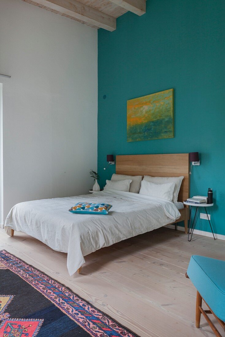 Schlichtes Bett im Schlafzimmer mit hoher Decke und blauer Wand