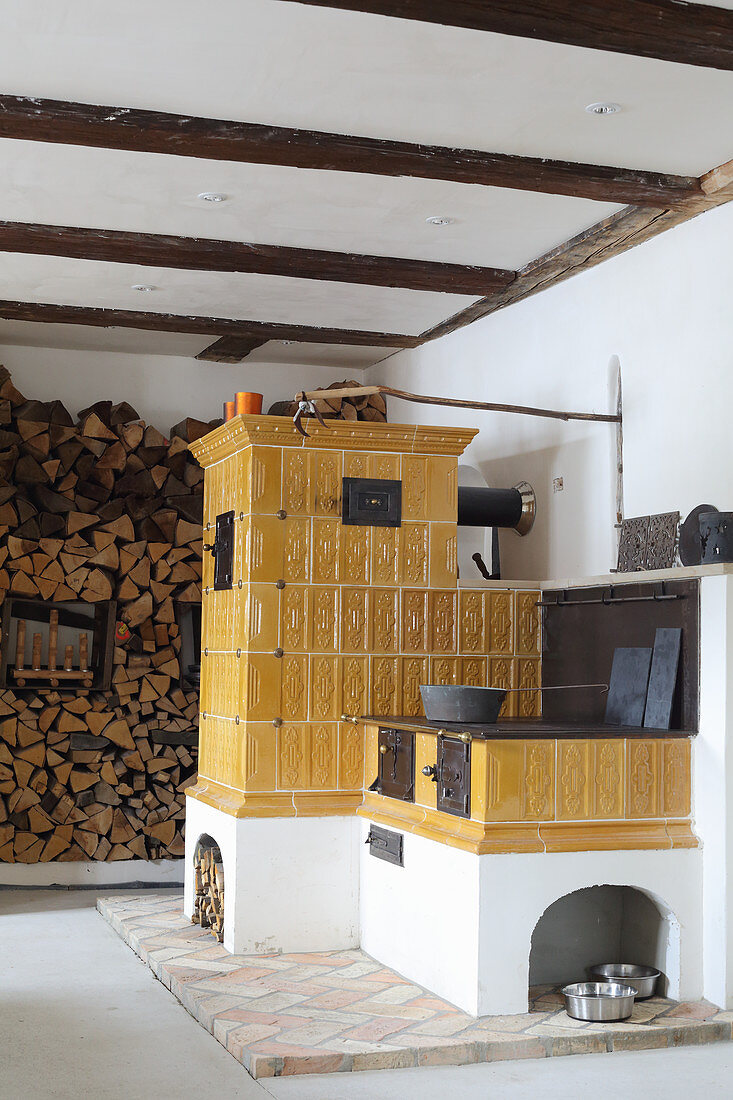 Alter gelber Kachelofen und Küchenofen neben Holzstapel