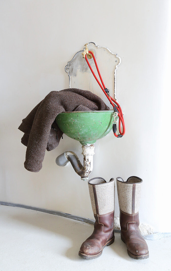 Leather boots below cardigan draped over old wall-mounted sink