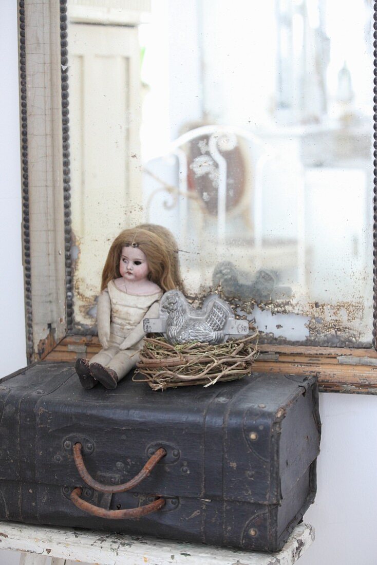 Puppe neben einem Nest mit Hühnerbackform auf altem Koffer