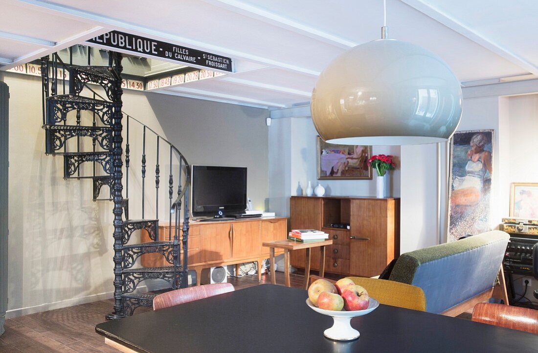 Blick über Esstisch in Wohnraum mit Retro-Flair und gusseiserner schwarzer Wendeltreppe