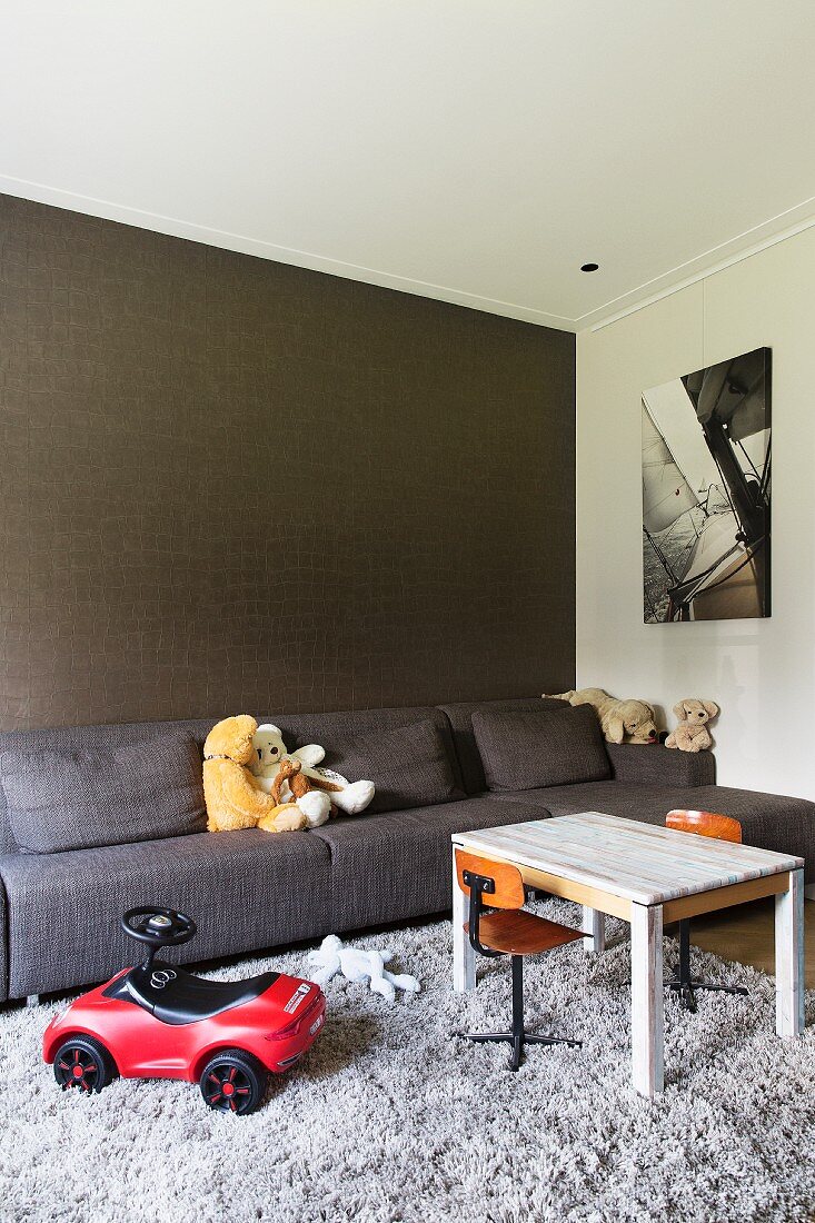 Toys, grey sofa and wall with structured surface in living room