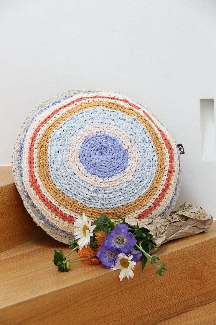 Flowers next to round cushion with crocheted cover made from T-shirt yarn