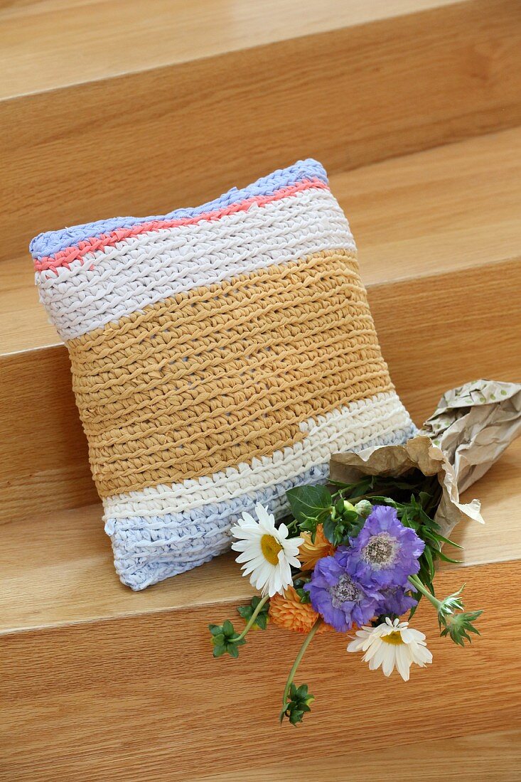 Flowers next to square cushion with crocheted cover made from T-shirt yarn