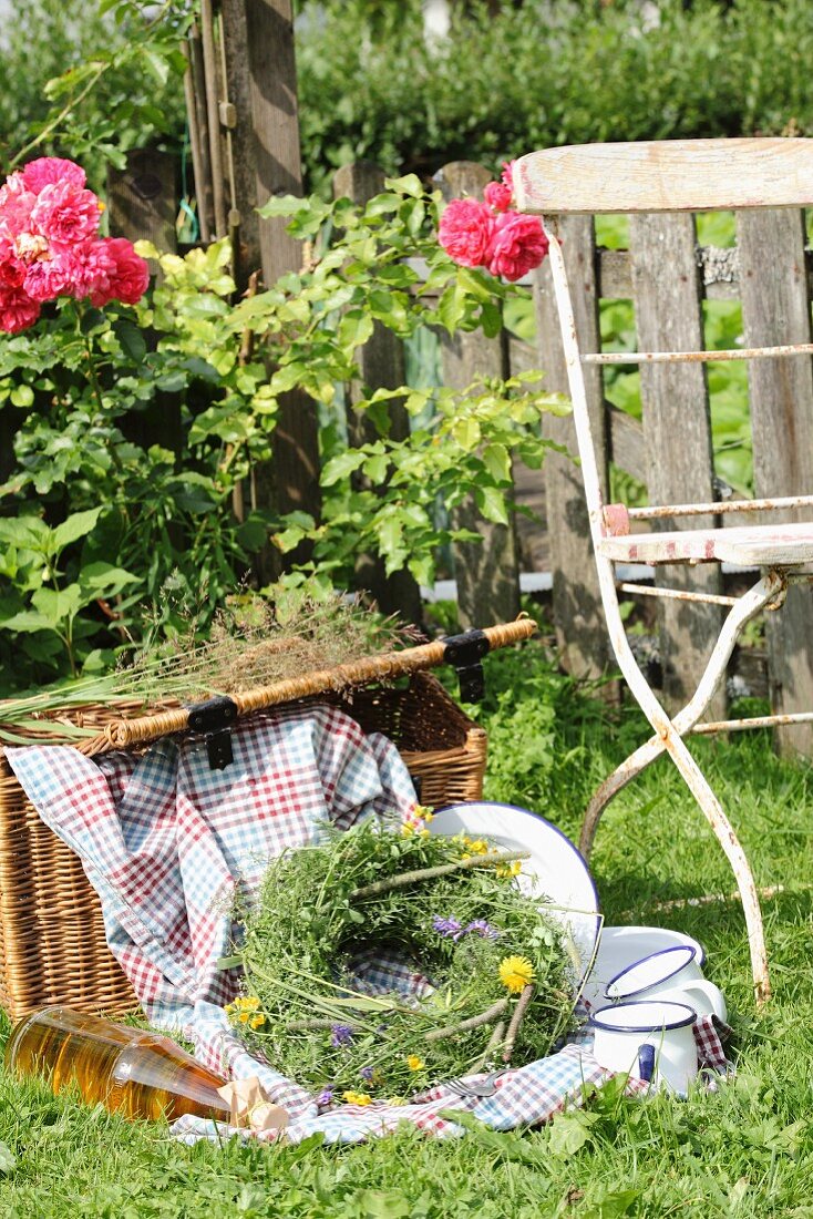 Picknickkorb mit Decke und Emaillegeschirr im Garten mit Wiesenblumenkranz
