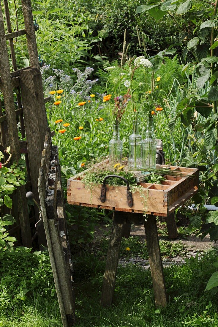 Vintage Holzkasten mit verschiedenen Blüten und Glasflaschen im ländlichen Garten