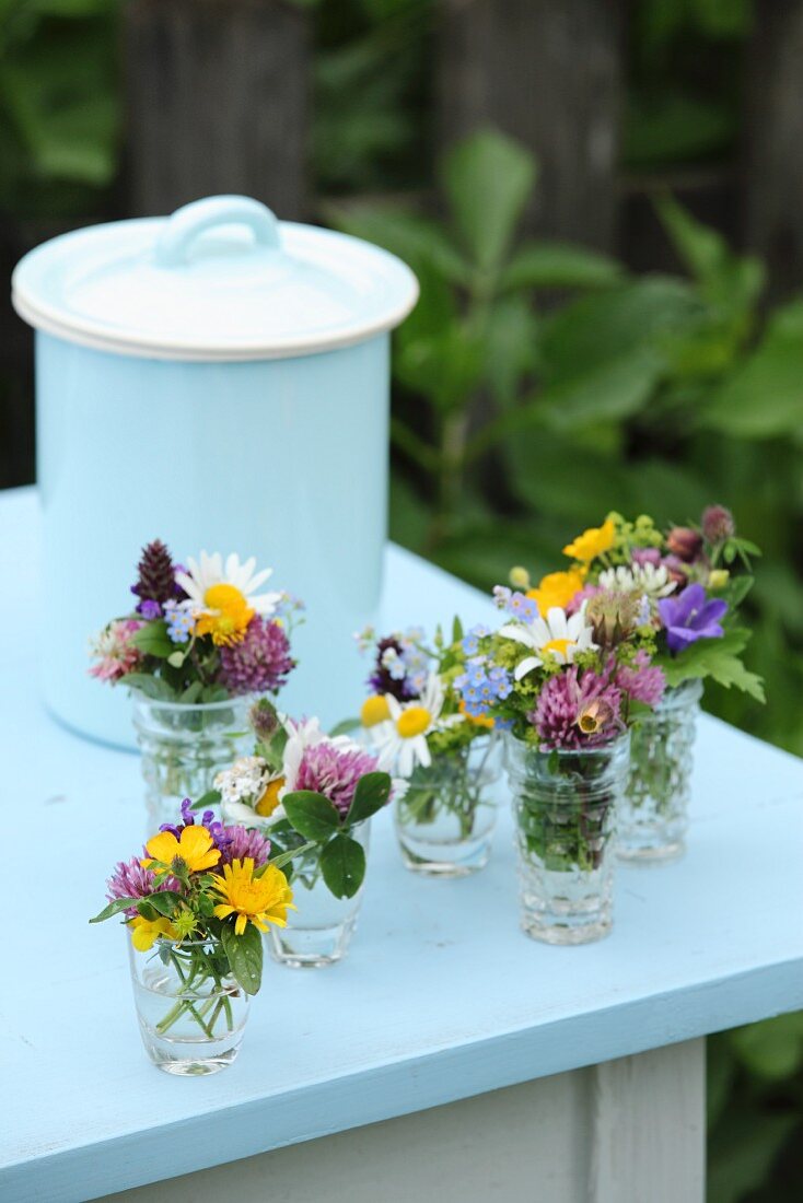 Bunte Wiesenblumensträusschen in Glasväschen auf hellblauem Tisch