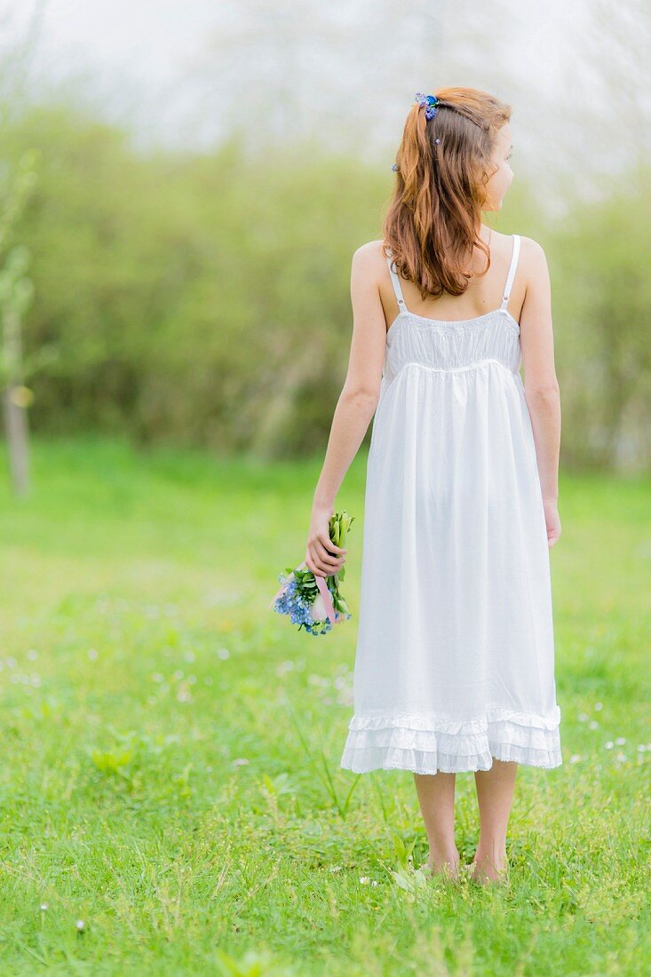 Girl wearing white summer dress holding posy on lawn