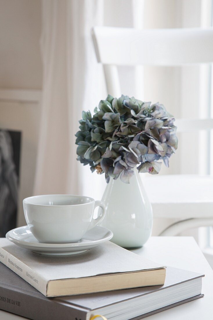Hydrangea in white vase and teacup on book
