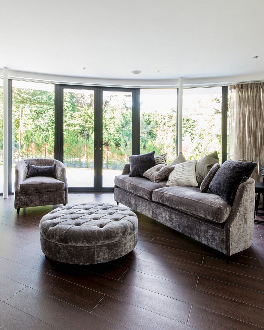 Velvet-upholstered furniture in living room with curved glass wall