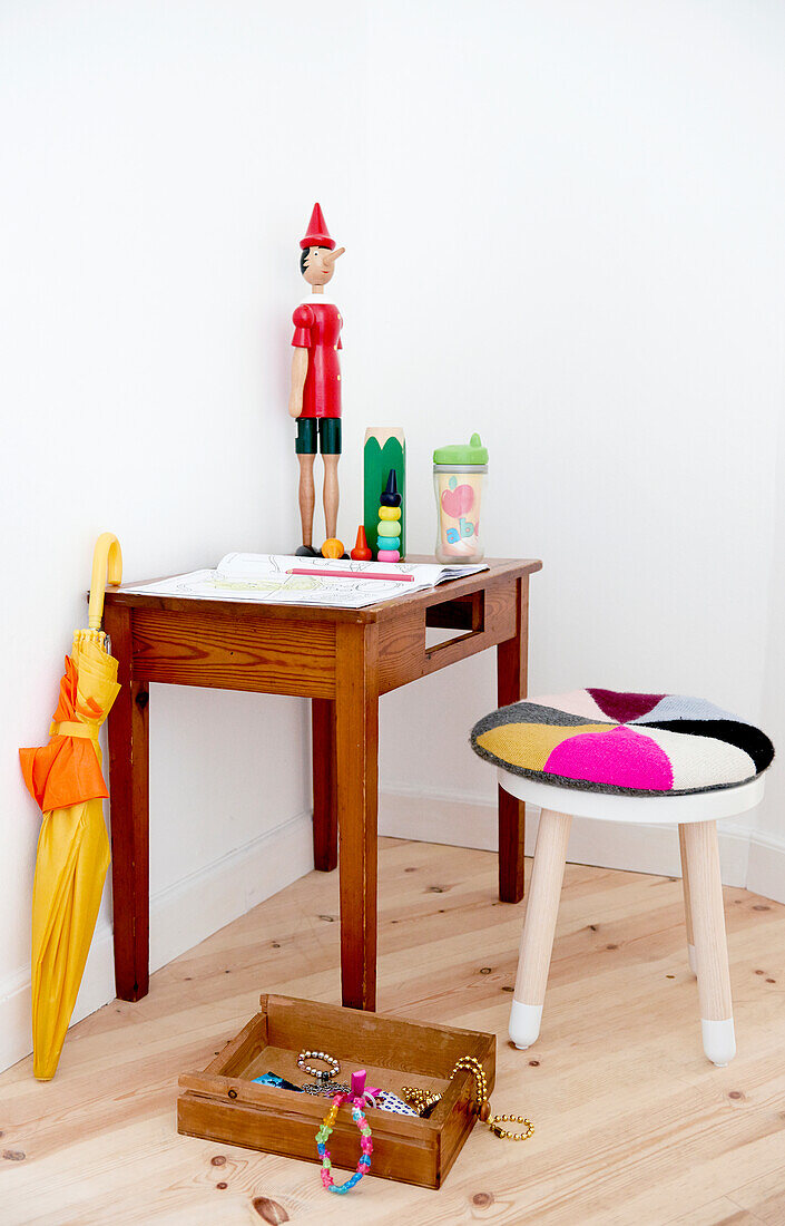 Toys and colouring book on table, umbrella, round stool with cushion and drawer full of jewellery in corner