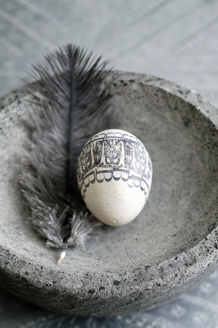 Mit schwarzem Ornament bedrucktes, ausgeblasenes Ei und Feder in Steinschale