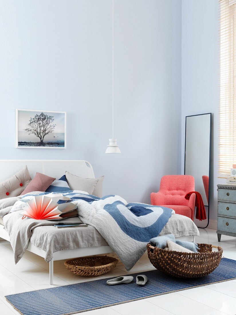 Schlafzimmer in Blautönen mit lachsfarbenem Polstersessel, Standspiegel und Körben beim Bett