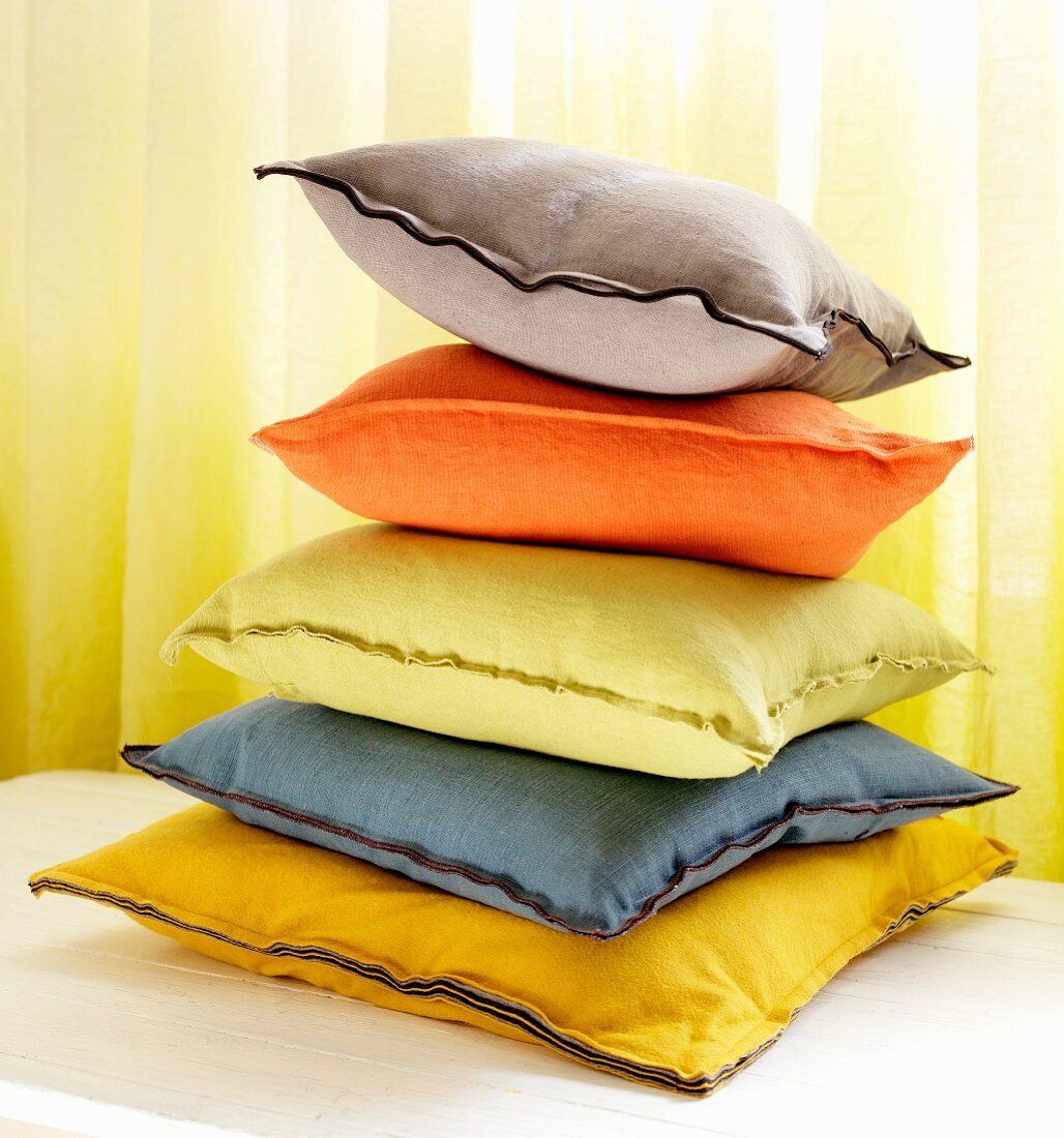 Stack of colourful cushions in front of yellow curtain