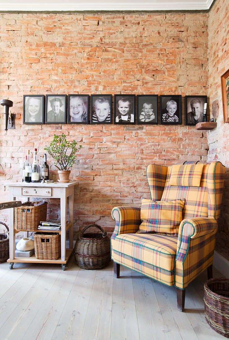 Tartan wing-back chair in front of family photos on brick wall