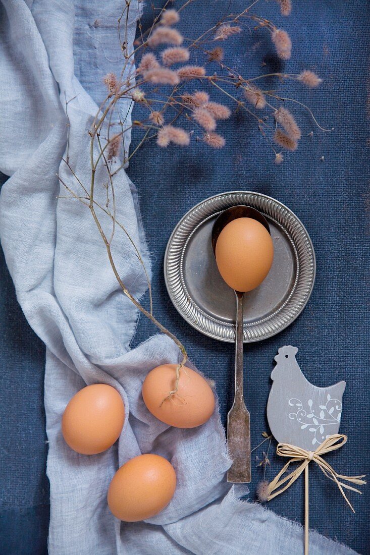 Deko-Huhn und Eier auf blauem Stoff, Vintage-Löffel und Zinnteller