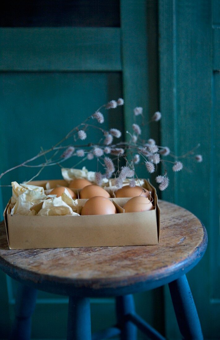 Vintage Pappschachtel mit Eiern und Trockenzweig auf Holzhocker