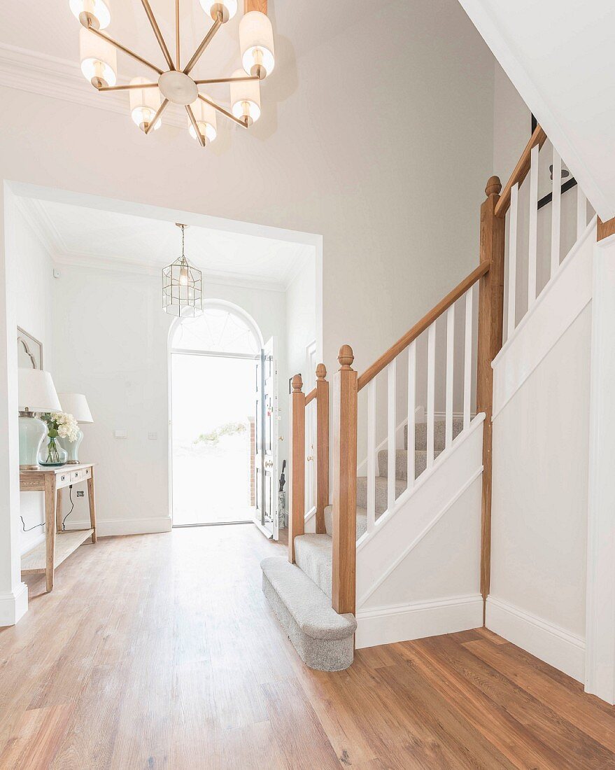 Treppenaufgang mit grauem Treppenteppich in eleganter Eingangsdiele mit geöffneter Haustür