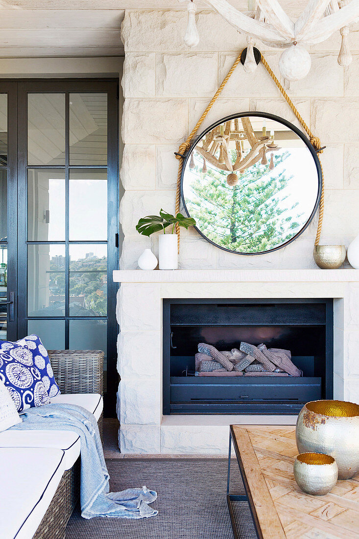 Round mirror hangs on the stone wall above the fireplace with rope