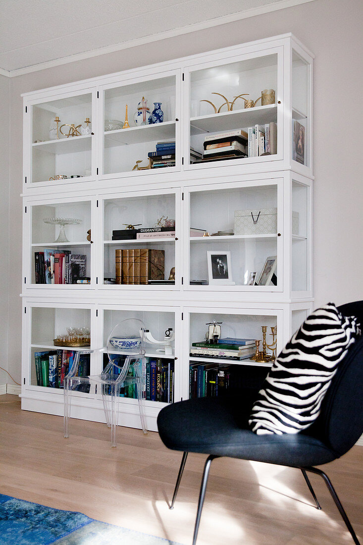Zebra-patterned cushion on black easy chair in front of glass-fronted cabinets