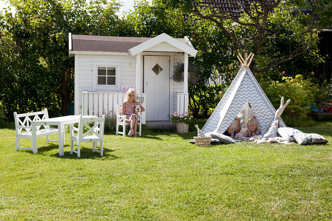 Wendy house, wigwam and children's furniture on lawn in sunny garden