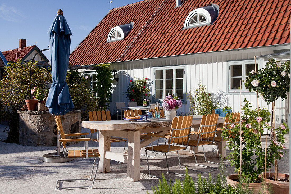 Langer Tisch und Stühle auf sonniger Terrasse vor dem Haus