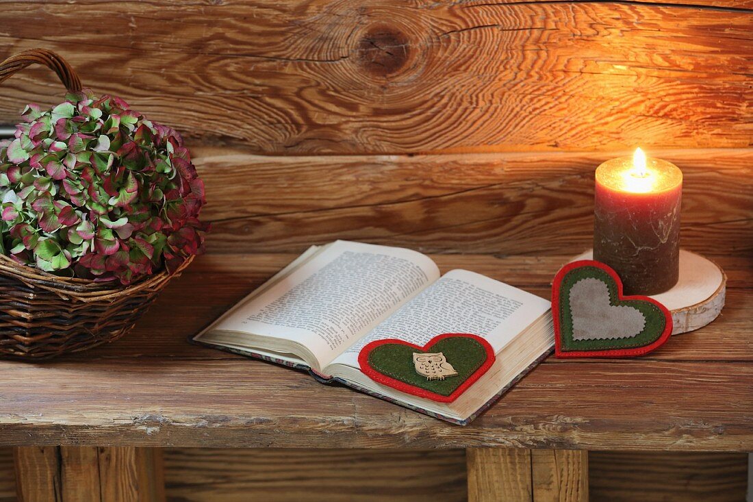 DIY-Lesezeichen aus Filz in Herzform neben brennender Kerze auf rustikaler Holzbank