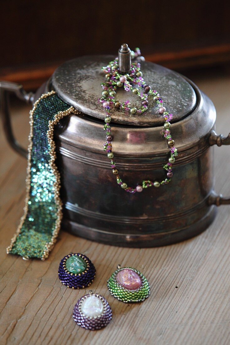 Vintage silver pot decorated with glass-bead jewellery and three necklace pendants
