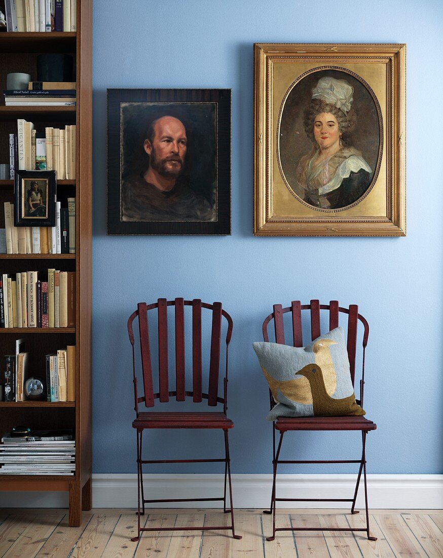 Zwei Portraitgemälde mit antikem Flair in verschiedenen Rahmen an hellblauer Wand