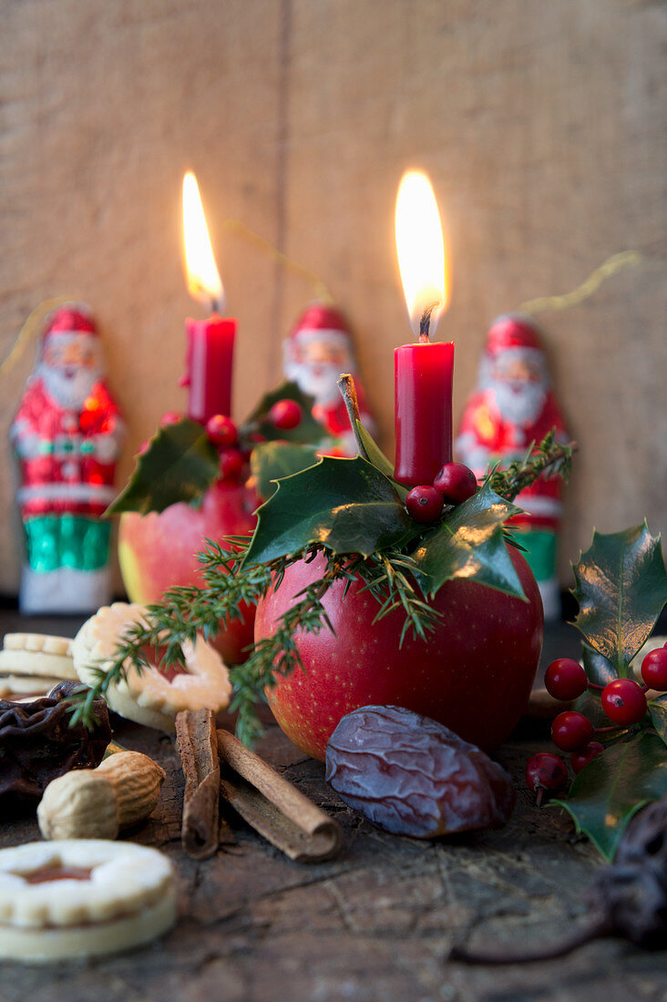 Christmas apples decorated with candles, larch cones and juniper sprigs, biscuits, chocolate Santas, dates and peanuts