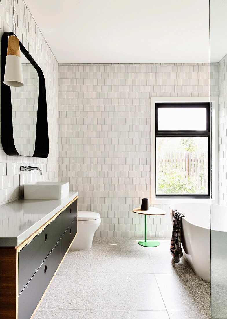 Badezimmer mit hellen Struktur-Fliesen an der Wand, Waschtischunterschrank und frei stehender Badewanne