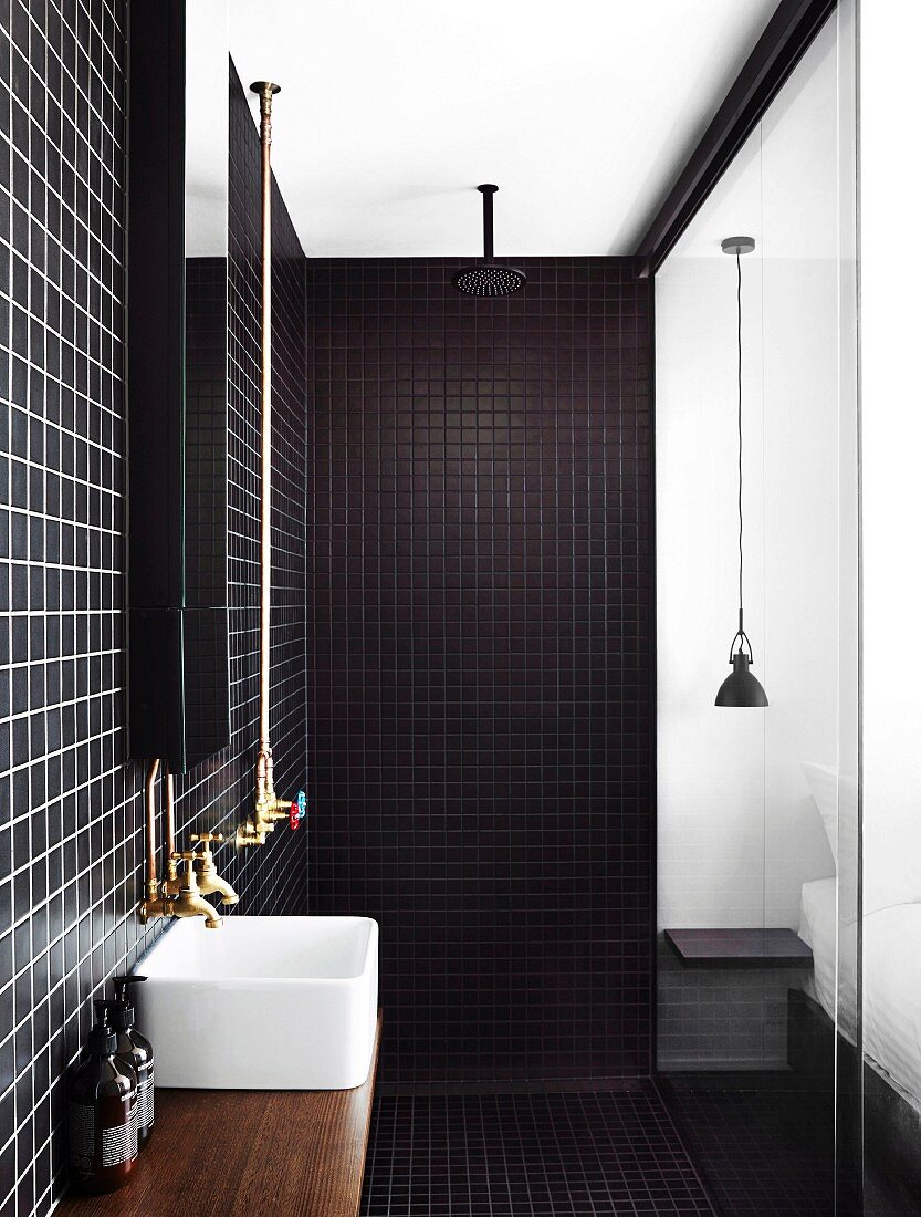 Moderner Duschbereich mit dunklen Wand- und Bodenfliesen, Aufsatzbecken und Glasabtrennung zum Schlafzimmer