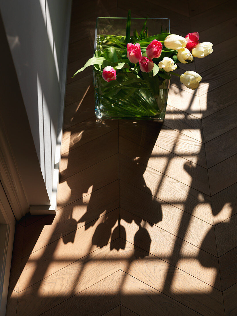 Strauß Tulpen in der Glasvase wirft Schatten auf den Holzboden