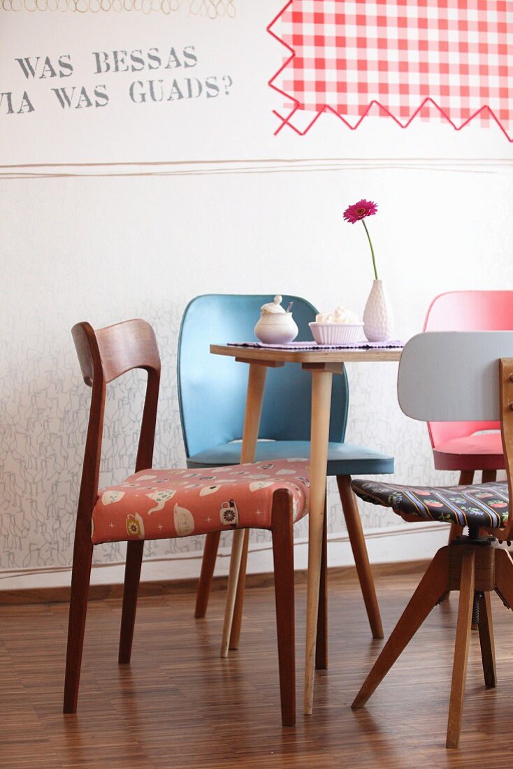 Various retro chairs around Gerbera, meringue and sugar bowl on table